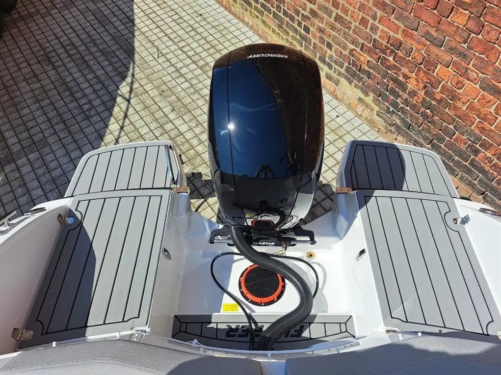 View from above of a boat deck with gray flooring, an engine, and a textured surface against a brick wall backdrop.